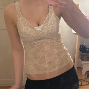 Vintage spetslinne - Säljer ett beige linne i spets med blommönster och v-ringad hals. Toppen är ärmlös och har en figurnära passform. 