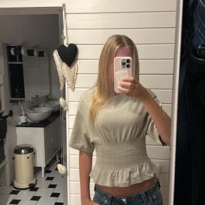Grön beige söt topp!!! - Säljer en beige croppad blus med bred resår i midjan och volang nertill. Toppen har korta ärmar och rund halsringning. Materialet känns mjukt och lätt, perfekt för en chill look. Snygg att styla med jeans eller kostymbyxor❣️❣️