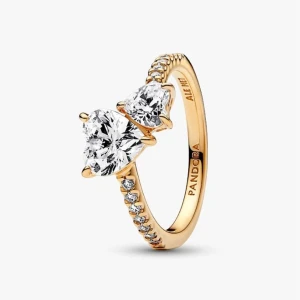 Pandora ring  - Ordinarie pris 1299kr. Helt ny och är helt oanvänd. Med orginal paket. Snygg guldfärgad ring från Pandora med två stora hjärtformade klara stenar i centrum och mindre gnistrande stenar längs bandet. Perfekt för dig som gillar bling och romantiska detaljer. Ringen har en elegant och modern design som verkligen sticker ut.