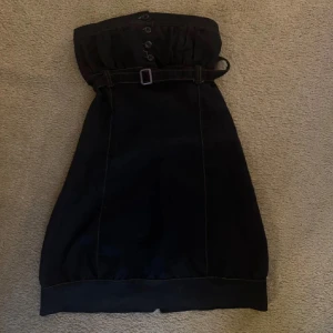 Mörkblå axelbandslös kortklänning med bälte - Mörkblå denim axelbandslös kortklänning med snygga knappar framtill och ett matchande bälte i midjan. Klänningen har rynkad överdel och markerad söm längs kanterna. Perfekt för dig som gillar stilrena och enkla plagg med coola detaljer. Jag har sytt in den själv, men går att sprätta upp, men därför har de är den inte helt perfekt på insidan!💗