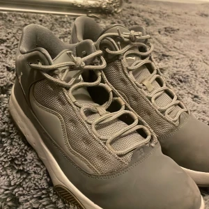 Grå Nike Jordan 1 sneakers strl 41 - Säljer ett par grå Nike Jordan 1 sneakers i storlek 41. Skorna har en snygg mesh-panel på sidorna, detaljerad snörning och en platt sula. De har en sportig vibe med diskret Jumpman-logga och siffran 23 på tån. Perfekta för dig som gillar stilrena och bekväma sneakers.