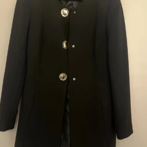 Svart kappa från Zara med stora knappar Storlek S - Säljer en svart kappa från Zara med stora, dekorativa silverfärgade knappar framtill. Kappan har rund halsringning, långärmad och klassisk rak passform, passar både höst och vår. 🍂  #zara 