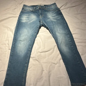 Blå raka jeans med ljusa slitningar - Snygga blå jeans med raka ben och ljusa slitningar på låren. Klassisk femficksmodell med knapp och dragkedja i gylfen. Perfekta för en avslappnad stil och passar till det mesta. Tillverkade i mjukt jeanstyg för skön känsla.