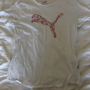 Vit Puma t-shirt  - Vit t-shirt från Puma i bomull med klassisk rosa Puma-logga på bröstet. Det står den är storlek L men sitter som en M (enligt mig). Använd 2-3 gånger så den ser ny ut. 