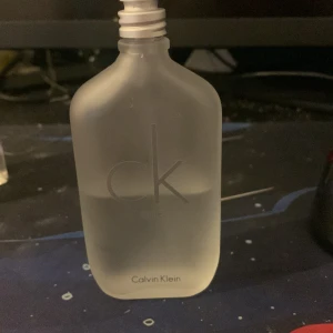 CK One unisex parfymflaska - Stilren och klassisk parfym från Calvin Klein. Flaskan har frostat glas och passar dig som gillar enkel design. Perfekt för dig som vill ha en ikonisk doft i samlingen. Volym och ingredienser syns ej på bilderna.