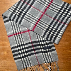 Klassisk Burberrys ullhalsduk – Grå, svart & röd - Tidlös Burberrys-halsduk i den klassiska rutiga designen. Mjuk, varm och elegant – passar både herr och dam. I fint vintage-skick. Timeless Burberrys wool scarf in the iconic check pattern. Soft, warm, and elegant – perfect for both men and women. In great vintage condition. 