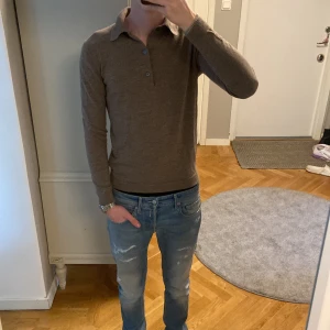 A Day's March stickad tröja - Snygg brun pikétröja från A Day's March i storlek S. Tröjan har klassisk krage, tre knappar framtill och är långärmad. Materialet är mjuk och tunn ull som känns skönt mot huden. Modellen är 187 lång. Perfekt för dig som gillar stilrena och enkla plagg. Skicka vid minsta fundering?