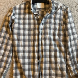 Rutig skjorta från Oscar Jacobson - Snygg rutig skjorta från Oscar Jacobson i grått och vitt. Skjortan har klassisk krage, knäppning framtill och långa ärmar. Perfekt för dig som gillar stilren och tidlös design. Tillverkad i mjuk bomull för en skön känsla hela dagen. Strl 38