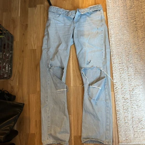 Ljusblå ripped jeans straight fit - Säljer ett par ljusblå jeans med raka ben och flera slitningar och hål på framsidan för en cool, avslappnad vibe. Klassisk femficksmodell och knappgylf. Perfekt för dig som gillar streetstyle och vill sticka ut.