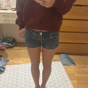 Blå denimshorts från ONLY, waist 25 - Säljer ett par blå denimshorts från ONLY med låg midja och klassisk femficksdesign. Shortsen har snygga detaljer med dubbla knappar och synliga sömmar. Perfekta för sommaren och har en tight passform.