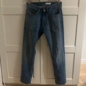 Tiger of Sweden blå jeans REX 28/32 - Blå jeans från Tiger of Sweden i modellen REX, med klassisk femficksdesign och raka ben. Jeansen har normal passform och är tillverkade i bomull. Snygg tvätt med subtila slitningar och detaljer som metallknapp och logopatch bak i midjan.