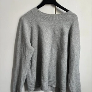 Grå stickad tröja - Mysig grå stickad tröja med bred ribbad krage och muddar. Perfekt för kyliga dagar och enkel att matcha med jeans eller kjol. Långärmad och i klassisk modell som funkar året om.