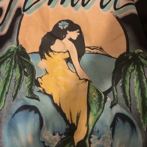 AMIRI tröja med färgglatt tryck - Snygg tröja från AMIRI med ett stort färgglatt tryck av en sjöjungfru, palmer och havsmotiv på framsidan. Tröjan har inslag av gult, grönt, blått och svart och är tillverkad i mjuk bomull. Perfekt statement piece för dig som vill sticka ut.