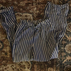 Blåvita randiga linnebyxor - Snygga blåvita linnebyxor med vertikala ränder och elastisk midja. Byxorna har en avslappnad passform och är perfekta för varma dagar. Materialet är lätt och luftigt, vilket gör dem sköna att bära. Passar mig som är 157!