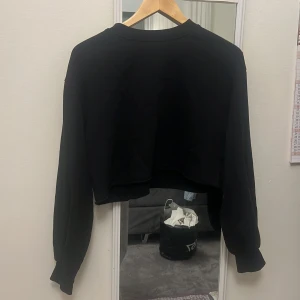 Svart croppad sweatshirt - Svart croppad sweatshirt med rund hals och långa ärmar. Tröjan har en loose passform och är perfekt för en avslappnad stil. Tillverkad i mjukt material som känns skönt mot huden.