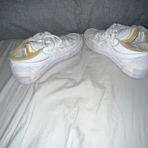 Nike Blazer Low vit sneaker - Nike Blazer Low sneakers i helvitt med klassisk snörning och rund tå. Skorna har en chunky platt sula och detaljer i vitt skinn samt textil. Snygg retrostil med orange Nike-logga på plösen. Perfekt för dig som gillar clean och sportig look.