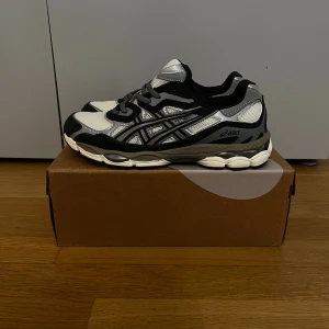 ASICS Gel-NYC Oatmeal Obsidian Grey - ASICS Gel-1090 sneakers med cool retrodesign i svart, grått och vitt. Ovandel i mesh och syntet med klassiska ASICS-stripes på sidorna. Platt sula med dämpning och rund tå. Perfekt för dig som gillar sportig stil och komfort. Snörning framtill för bästa passform.