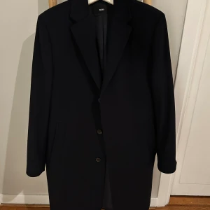 Mörkblå Hugo Boss rock i kashmirull *50* - Stilren rock från Hugo Boss, tillverkad i exklusiv kashmirull och ullblandning. Klassisk rak modell med två knappar framtill, diskreta fickor och elegant foder med innerficka. Perfekt för dig som vill ha en snygg och tidlös look. Sömmen i höger innnerficka har lossnat lite men det är lätt åtgärdat.