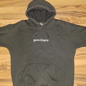 Svart hoodie från Palm Angels  - Svart hoodie från Palm Angels med stor vit logga på ryggen och mindre logga på bröstet. Tröjan har huva med snörning, känguruficka och är tillverkad i mjuk bomull. Super snygg och sitter bra! Hör av er vid frågor
