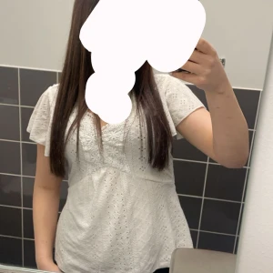 Vit blus med spetsdetaljer - Säljer en söt vit blus med v-ringning och korta ärmar. Blusen har broderade spetsdetaljer och ett luftigt, lätt material som passar perfekt till varmare dagar. Den har en feminin och avslappnad passform.