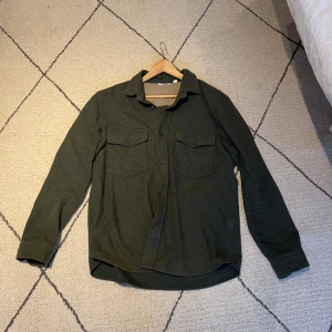 Mörkgrön overshirt med fickor från Dobber - Snygg mörkgrön overshirt med klassisk krage och två stora bröstfickor med knappar, från Dobber.