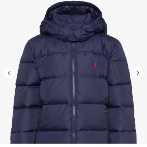 Mörkblå pufferjacka från Polo Ralph Lauren - Säljer en mörkblå pufferjacka från Polo Ralph Lauren med huva och dragkedja framtill. Jackan har det klassiska röda Polo-logot broderat på bröstet och är perfekt för kalla dagar. Den är quiltad och har en oversized look.