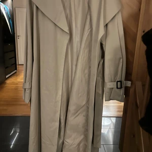 Beige trenchcoat från Stories S - Snygg beige trenchcoat från Stories i storlek S. Jackan har breda slag, bälte i midjan och spännen vid ärmsluten för extra stil. Perfekt för dig som gillar klassisk look mer modern touch. Materialet är mjukt och lätt, passar grymt under vår och höst.