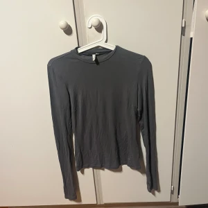 Grå långärmad topp från NLY Trend - Säljer en enkel och stilren grå långärmad topp från NLY Trend i storlek XS. Modellen är tight och har rund halsringning. Perfekt att matcha med jeans eller kjol för en clean look. Materialet är mjukt och känns skönt mot huden.