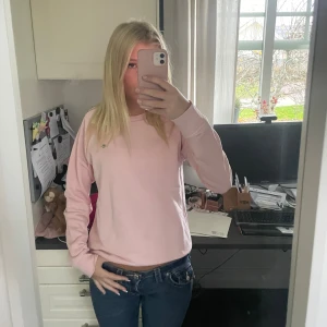Ljusrosa sweatshirt från GANT - Säljer en ljusrosa sweatshirt från GANT med klassisk rund hals och diskret logga broderad på bröstet. Tröjan har ribbade muddar vid hals, ärmslut och nederkant. Mjuk bomullskvalitet och normal passform, perfekt för en chill och stilren look.