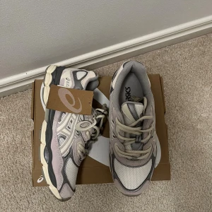 Asics gel nyc  - Snygga Asics sneakers med chunky sula i grått och beige. Ovandelen är i mesh och syntet med coola paneler och detaljer. Skorna har snörning och rund tå, samt en tag med Asics-loggan. Perfekta för dig som gillar sportig och trendig stil.