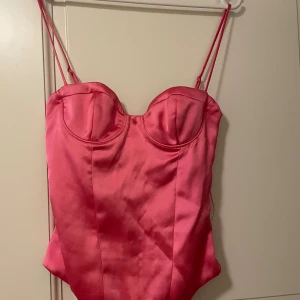 Rosa satin body från Zara - Säljer en snygg rosa korsettopp från Zara i glansigt satinmaterial. Toppen har tunna axelband, markerade kupor och figurnära passform. Perfekt för dig som vill sticka ut med en trendig och feminin look.