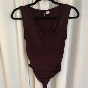 Vinröd ärmlös body från Divided - Säljer en vinröd ärmlös body från Divided med snygg v-ringning och spetsdetaljer längs halsen