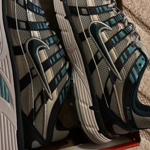 Nike P-6000 sneakers silver/blå - Nike P-6000 sneakers i silver och blå med svarta detaljer. Skorna har mesh-paneler för bra ventilation, syntetiska överdrag och en chunky, mönstrad sula. Swoosh-logga på sidan och snörning framtill. Perfekt för dig som gillar retrovibe och sportig stil.