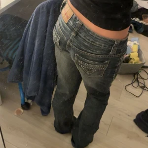 Jad'K Way jeans med nitar och broderi - Säljer ett par mörkblå bootcut jeans från Jad'K Way med snygga slitningar och coola nitar på bakfickorna. Jeansen har låg midja och klassisk femficksmodell. Materialet är jeans med broderade detaljer framtill och dekorativa sömmar. Innerbenslängden är ca 80 och midjemåttet är ca 40🫶🏼 Priset går att diskutera!!🥰