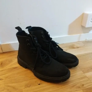 Svarta boots från Pier One, storlek 40 - Svarta boots från Pier One med grov sula och snörning framtill. Skorna har rund tå och är tillverkade i mocka med detaljer i syntet. Perfekt för dig som gillar en robust och stilren look. Passar dig som vill ha boots med lite edge.