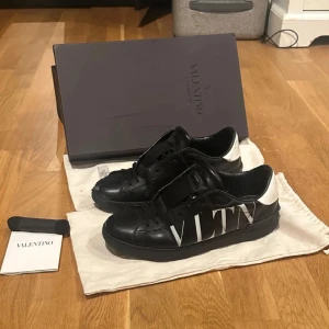Valentino skor - Säljer ett par svarta Valentino Garavani sneakers med vit VLTN-logga på sidan och vit häl. Skorna har snörning och platt sula, och är tillverkade i skinn. Kommer med originalkartong och dustbag och kvitto