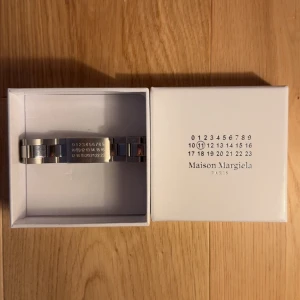 Maison Margiela silver armband - Stilrent armband från Maison Margiela i silverfärgat metall med deras ikoniska siffror ingraverade på plattan. Länkkonstruktion ger en cool och modern vibe, perfekt för dig som gillar minimalistisk design med edge. Kommer i original ask.