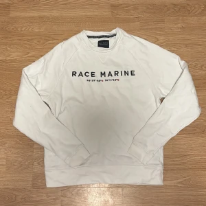Vit sweatshirt från Race Marine S - Vit sweatshirt från Race Marine med tryck på bröstet och koordinater. Tröjan har rund hals, långa ärmar och ribbade muddar. Hör av vid intresse!