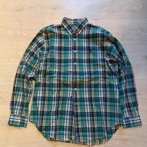 Rutig skjorta från Ralph Lauren M - Snygg rutig skjorta från Ralph Lauren i klassisk fit. Skjortan har gröna, blå, gula och vita toner med lila broderad logga på bröstet. Långärmad med knappar framtill och krage. Perfekt för dig som gillar preppy stil och vill ha något som sticker ut.