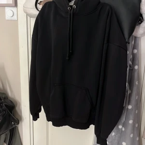 Svart hoodie från Bikbok med huva - Svart hoodie från Bikbok i storlek S. Tröjan har en stor huva med snörning och en klassisk magficka framtill. Modellen är loose fit med långa ärmar och ribbade muddar. Perfekt för chill dagar och enkel att matcha med jeans eller leggings.