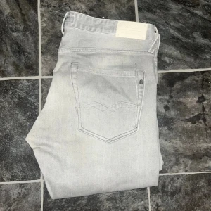 Replay jeans - Snygga ljusgrå jeans från Replay med klassisk femficksdesign och diskret Replay-logga på bakfickan. Jeansen har slim fit-passning och raka ben. JAG SKICKAR EJ FLER BILDER NÄR JAG BÄR JEANSEN! för storleksguide hänvisar jag till måtten och för bättre inblick i passformen rekommenderar jag att googla på modellnamnet. Jeansen kan vara uppsydda utan att jag noterat det så kolla måtten noggrant :) Midja 46cm, längd 100cm. OBS se defekt på sista bilden. 39