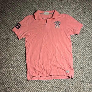 Rosa äldre Peak Performance piké M - Snygg rosa pikétröja från Peak Performance med klassisk krage och korta ärmar. Broderad logga på bröstet och siffra på ärmen. Sjukt snygg för en avslappnad och sportig look.