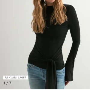 SÖKER I XS ELR S - Snygg svart långärmad topp med rund hals och coolt knyt i midjan. Modellen är slim och har långa ärmar med lätt utsvängd form. Perfekt att styla med jeans eller kjol för en trendig look.