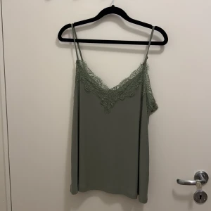 Grön linnetopp med spets från Amisu - Snygg ljusgrön linnetopp från Amisu med tunna axelband och v-ringning dekorerad med spets. Perfekt för sommaren och enkel att styla till olika looks. Toppens material känns mjukt och lätt mot huden.