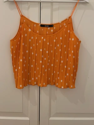 Orange prickig linnetopp från Bik Bok - Säljer en orange linnetopp från Bik Bok i storlek M. Toppen har vita prickar, tunna axelband och är plisserad för en cool struktur. Perfekt för varma dagar och har en luftig, loose passform. Materialet känns som lätt polyester.