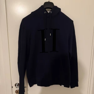 Mörkblå hoodie från Les deux med tryck - Snygg mörkblå hoodie från H&M med stor svart H-tryck på bröstet. Tröjan har huva med snörning och en klassisk känguruficka framtill. Perfekt för dig som gillar en enkel men stilren look.