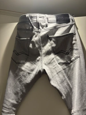 Replay ljusgrå jeans med skinny fit - Säljer ett par ljusgrå Replay jeans med skinny passform. Jeansen har klassisk femficksdesign, svarta kontrastsömmar och Replay-logga på bakfickan. Materialet är mjukt jeans och midjan är normal. Perfekt för dig som gillar stilrena och moderna jeans. Midjan är i storlek 31 och längden i storlek 32. Pris går att diskuteras och det är bara att höra av dig om du har frågor.