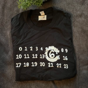 Svart t-shirt Maison Margiela 6 - Tja, jag säljer enSvart t-shirt från Maison Margiela med ikoniskt tryck av siffror och en stor 6:a i vitt på bröstet. Rund hals och klassisk passform. Materialet är mjuk bomull som känns skön mot huden. Perfekt för dig som gillar streetwear och coola designer.