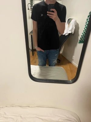 Svart CK t-shirt med kort ärm - Säljer en svart t-shirt från Calvin Klein med diskret CK-logga på bröstet. T-shirten har rund hals och korta ärmar, perfekt för en clean och stilren look. Materialet känns mjukt och bekvämt mot huden. Passar dig som gillar enkel och snygg design.