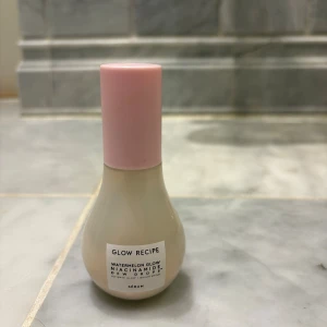 Glow Recipe Watermelon Glow Serum - Glow Recipe Watermelon Glow Niacinamide Dew Drops serum i en rund, droppformad flaska med ljusrosa pump och lock. Flaskan är genomskinlig med vit etikett och innehåller ett ljusrosa serum som ger glow och lyster till huden.